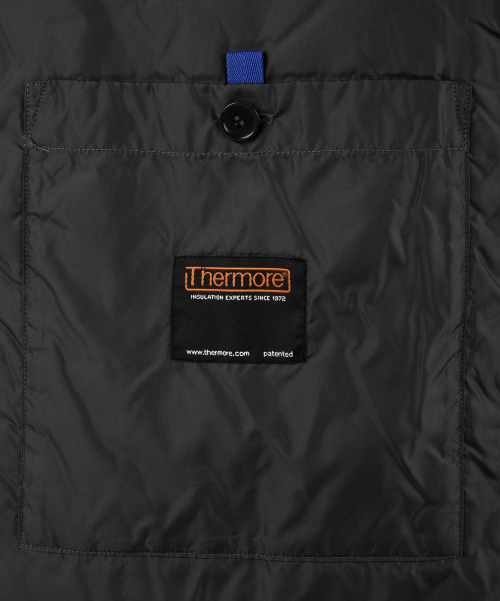 Dettaglio della tasca con bottone della camicia Compton grigia da uomo  e etichette riguardo l'imbottitura utilizzata che protegge dal freddo.